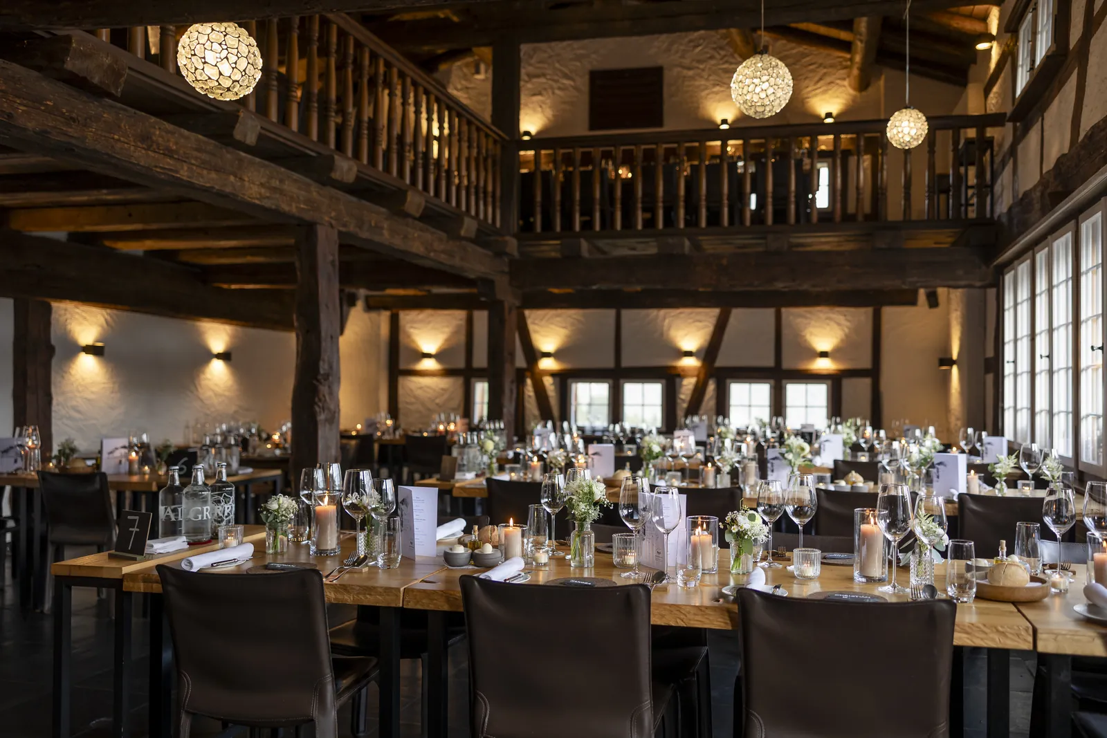 Festlich gedeckte Hochzeitstafel unter alten Holzbalken, Kerzenlicht und weisse Blumen
