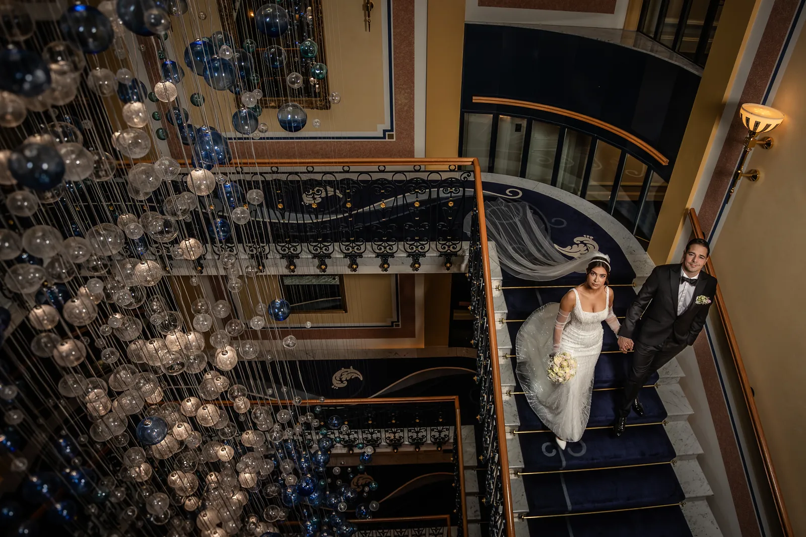 Brautpaar im Treppenhaus des Grand Hotel Quellenhof von oben, mit Glaskugel-Leuchter