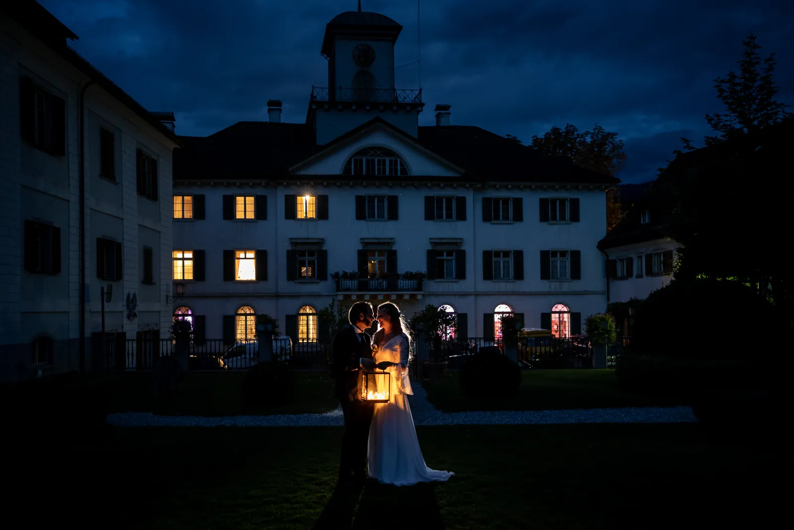 Brautpaar mit Laterne vor der beleuchteten Fassade von Schloss Reichenau am Abend