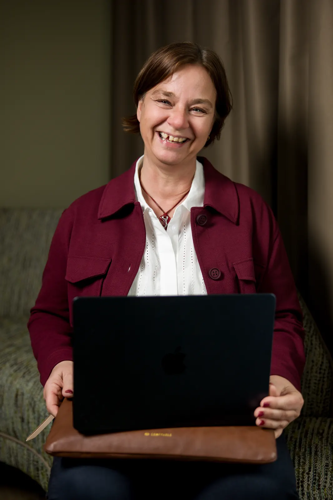 Unternehmerin sitzt mit Laptop auf dem Sofa und lacht, Branding-Bild für die Website