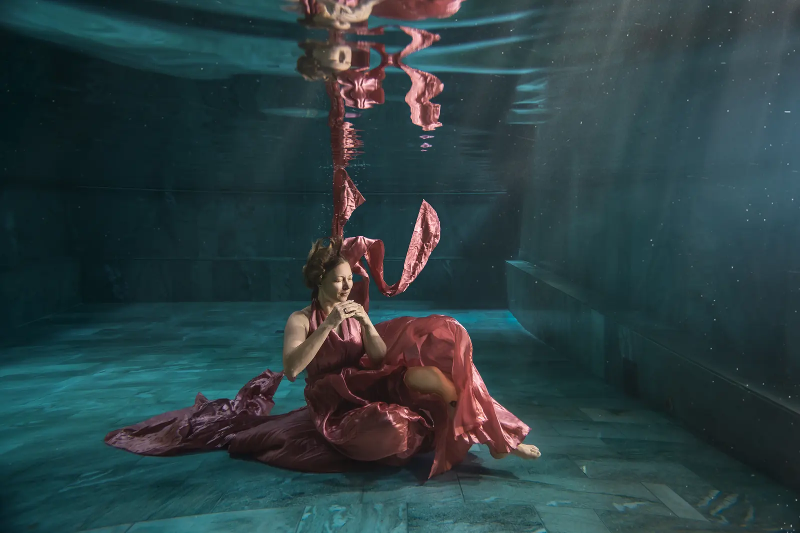 Frau im rosé Kleid sitzt auf dem Beckenboden, Stoff und Spiegelung an der Wasseroberfläche
