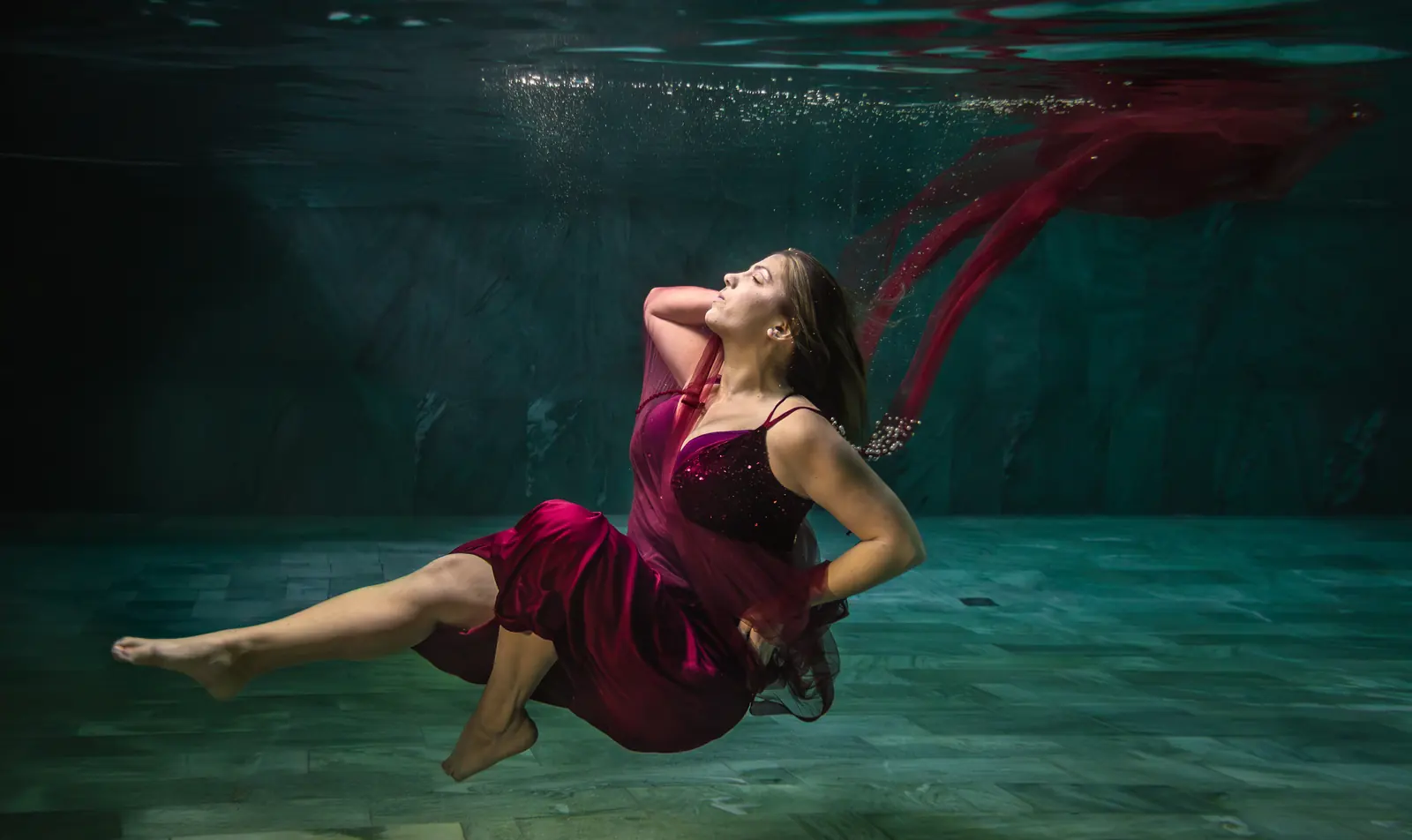 Frau im weinroten Kleid schwebt mit wehendem Tuch unter Wasser