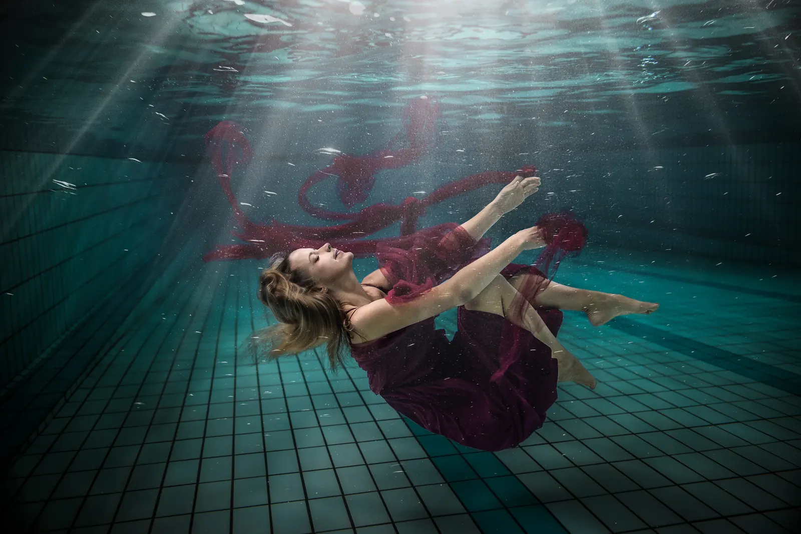 Frau schwebt rücklings unter Wasser, rotes Tuch umspielt ihren Körper