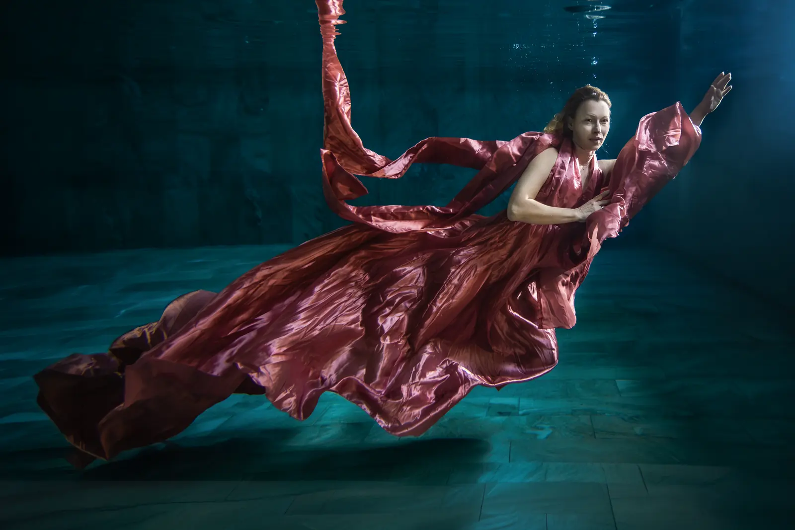 Frau im roséfarbenen Kleid schwebt unter Wasser und blickt in die Kamera – echtes Unterwasser-Portrait, keine KI