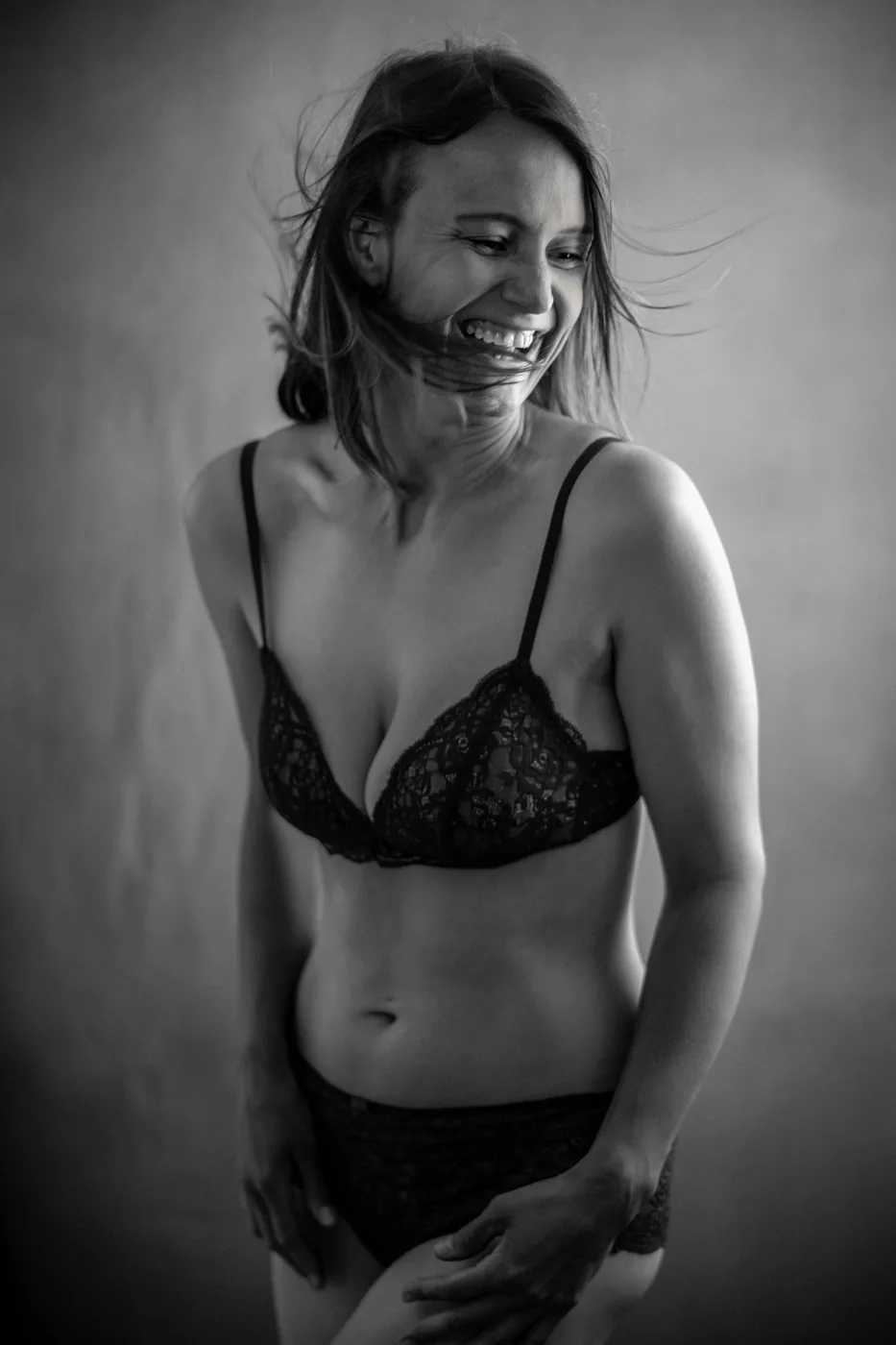 Lachende Frau in schwarzer Spitzenwäsche, Haare im Wind – Boudoir-Portrait