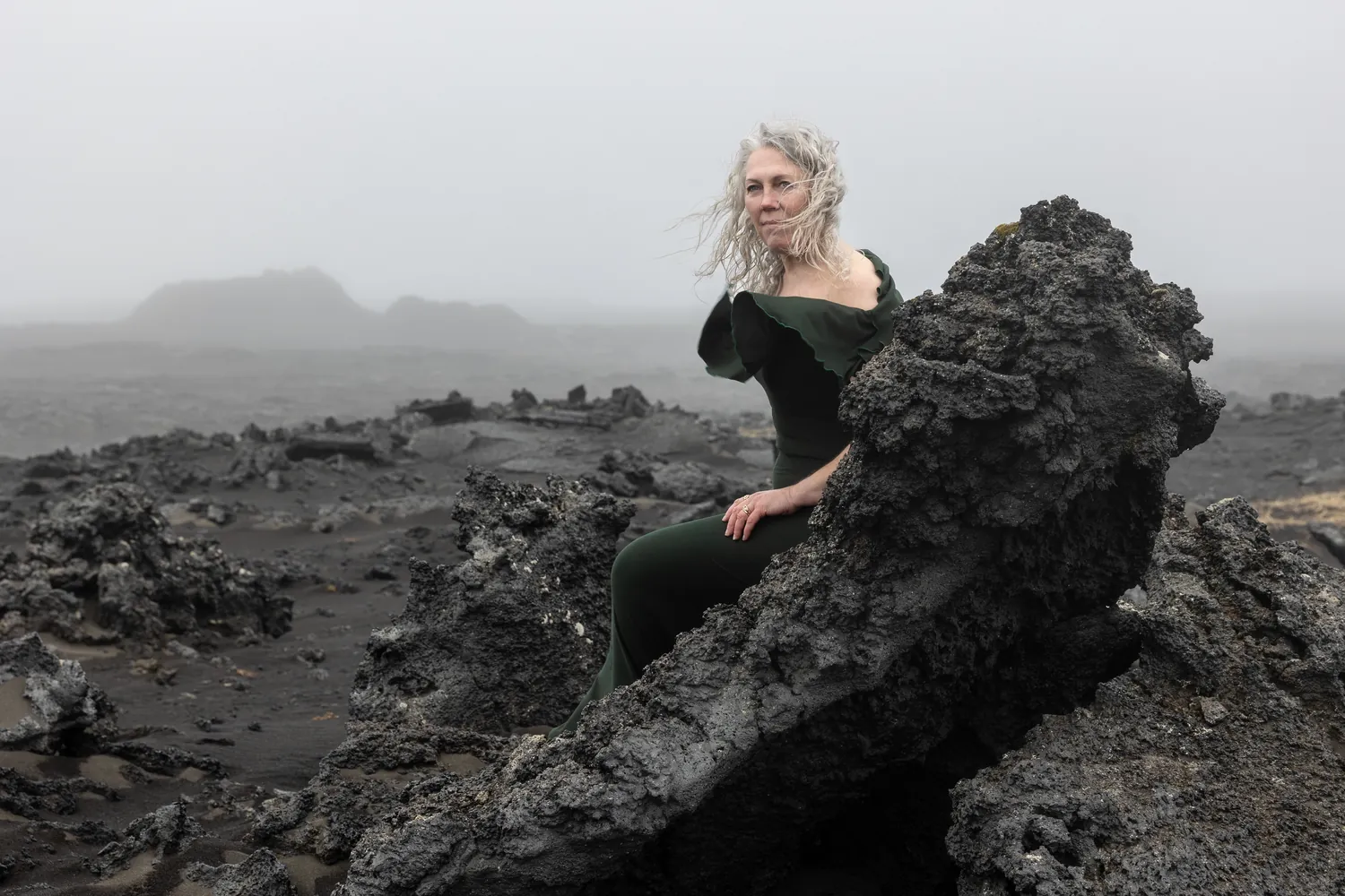 Frau im grünen Kleid auf schwarzem Lavagestein in Island