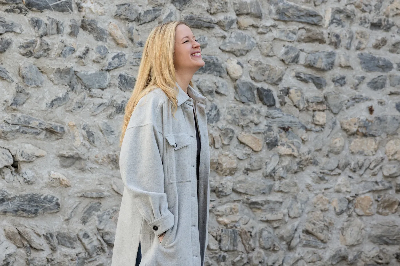 Frau lacht ausgelassen vor Natursteinmauer – Personal-Branding-Fotografie